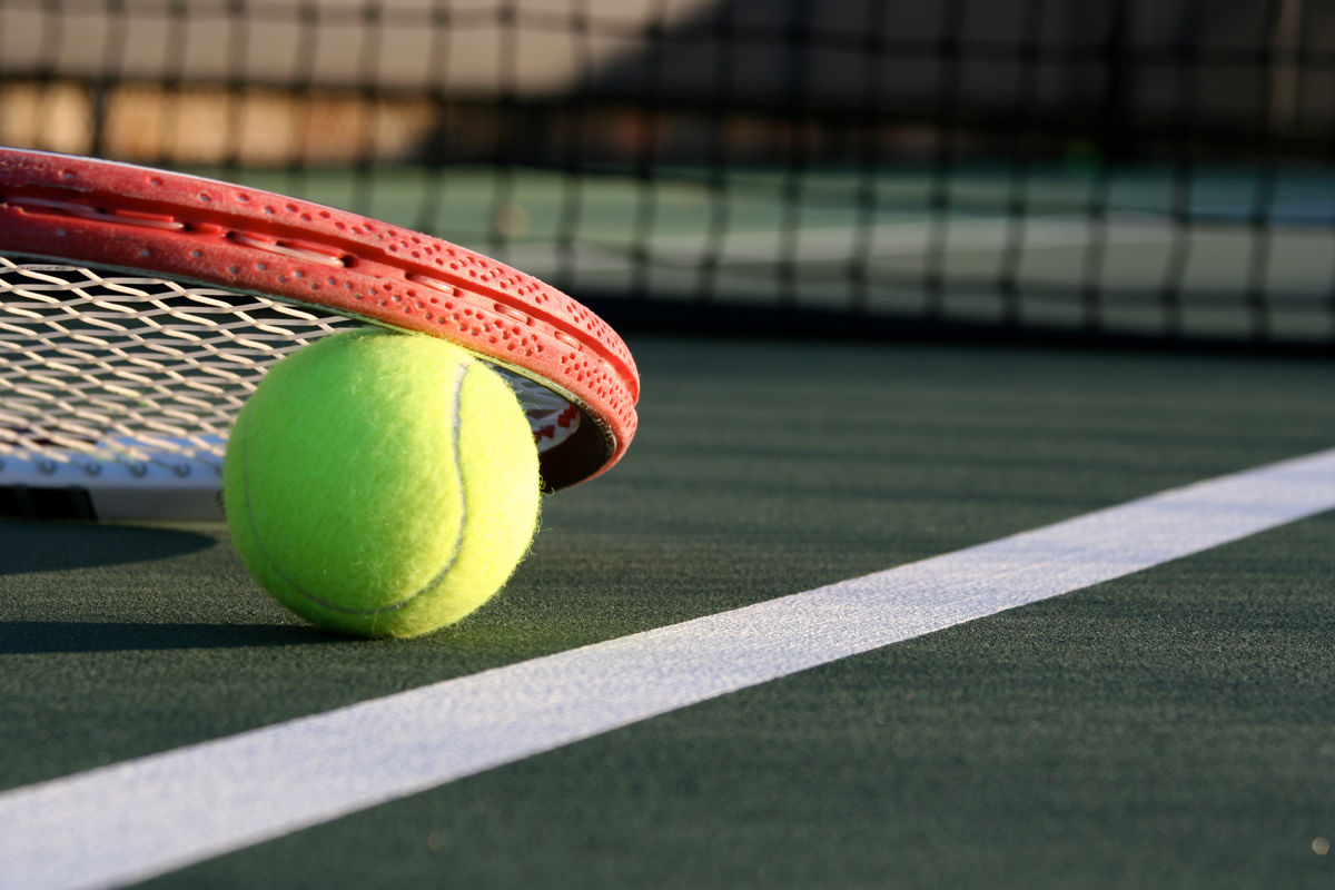 Närbild på ett tennisrack och en tennisboll på en tennisplan.